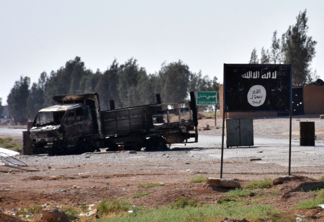 A general view shows a burnt out vehicle next to a banner bearing the Islamic State group's flag in the village of Dibsiafnan on the western outskirts of the Islamist's Syrian bastion of Raqa, after Syrian pro-government forces entered the area on June 11, 2017.