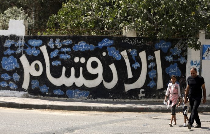 A Palestinian man and his daughter walk past a graffiti reading in Arabic ''Division'' in Gaza City, on September 17, 2017, after Hamas announced it had agreed to steps toward resolving a decade-long split with the Fatah movement and was ready to hold elections.