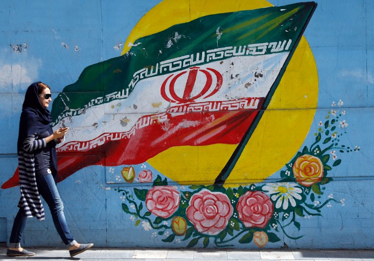 An Iranian woman walks past a mural of the Iranian flag in the capital Tehran, on October 14, 2017.