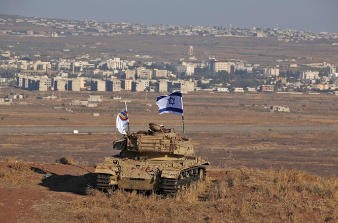 An Israeli flag flutters above the wreckage of an Israeli tank overlooking the border with Syria, on October 18, 2017.