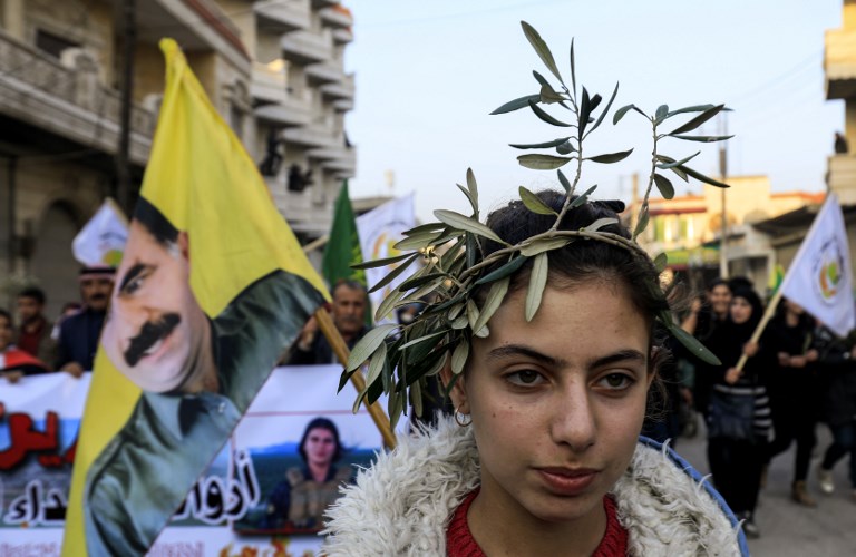 A woman wears a laurel of olive branches on her head as she marches with a flag bearing the portrait of Kurdistan Worker's Party (PKK) leader Abdullah Ocalan, ahead of a procession of Syrian Kurds, Arabs, and Syriacs bussed in from across northern Syria, in the Kurdish town of Jandairis near the Syrian-Turkish border, and 18 kilometres southwest of Afrin, on February 6, 2018.