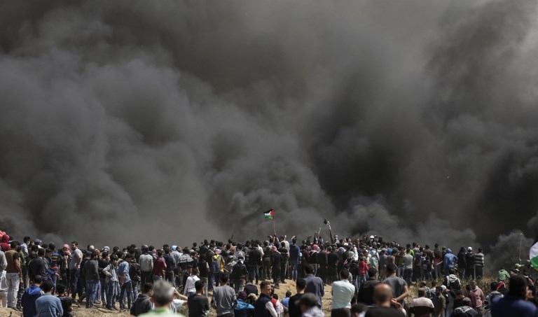 Palestinian men wave their national flags as smoke billows from burning tyres at the Israel-Gaza border during a protest, east of Gaza City in the Gaza strip, on April 6, 2018.