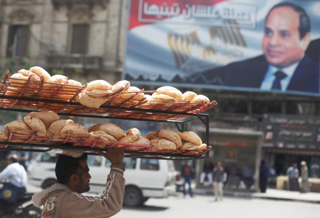 A man carries breads on his head along a busy street near a banner for Egypt's President Abdel Fattah al-Sisi after election results in Cairo. April 3, 2018.