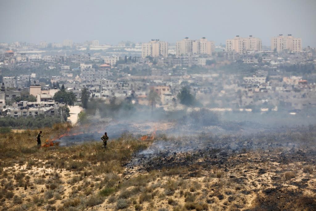 Israeli soldiers are seen near fire burns in scrubland in Israel near the Gaza Strip, in an area where Palestinians have been causing blazes by flying kites and balloons loaded with flammable material across the border between Israel and the Gaza Strip June 8, 2018.