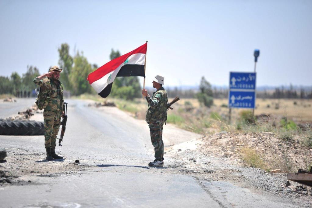 A member of forces loyal to Syria's President Bashar al-Assad holds the national flag as another one gestures in al-Ghariya al-Gharbiya in Deraa province, Syria in this handout released on June 30, 2018.