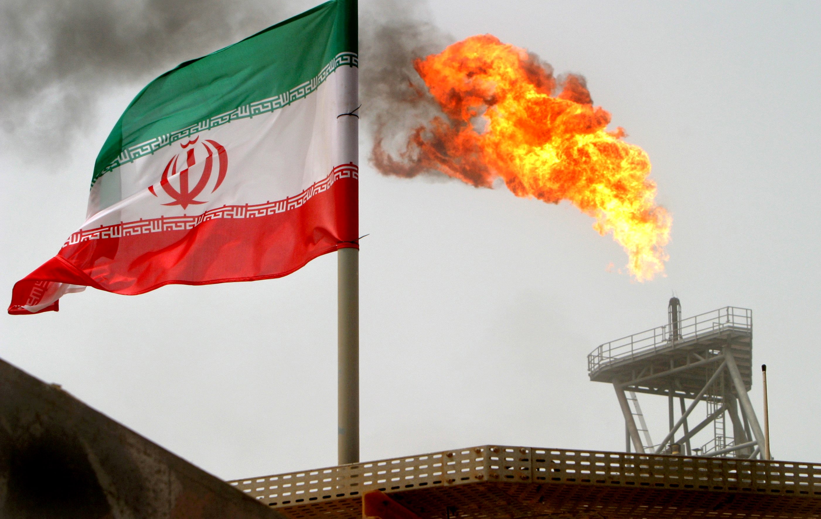A gas flare on an oil production platform in the Soroush oil fields is seen alongside an Iranian flag in the Persian Gulf, Iran, July 25, 2005.