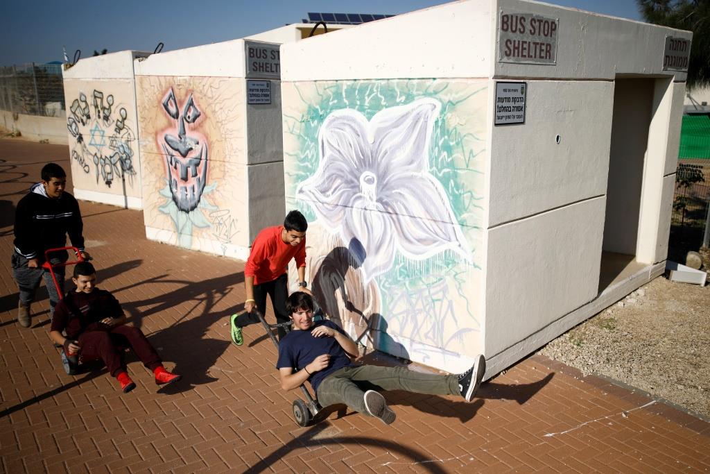 Teenagers drive each other in hand trucks next to bus stop bomb shelters in the southern city of Sderot, January 8, 2018.