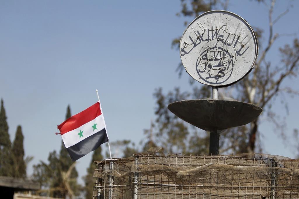 A Syrian national flag flutters next to the Islamic State's slogan at a roundabout where executions were carried out by ISIS militants in the city of Palmyra, in Homs Governorate, Syria. April 1, 2016.