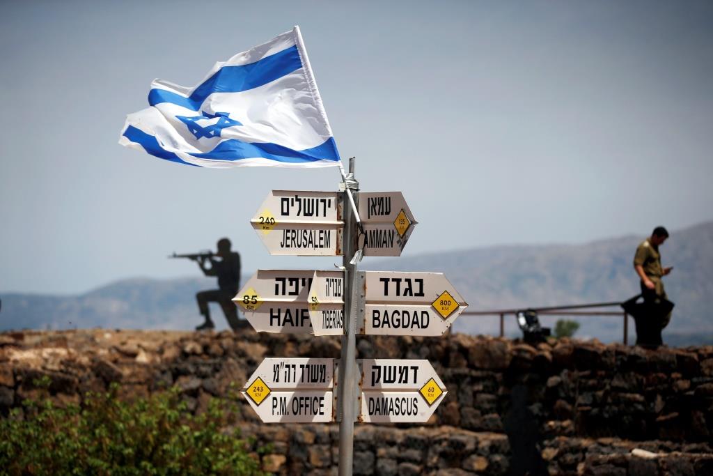 An Israeli soldier stands next to signs pointing out distances to different cities, on Mount Bental, an observation point in the Israeli Golan Heights that overlooks the Syrian side of the Quneitra crossing, May 10, 2018.