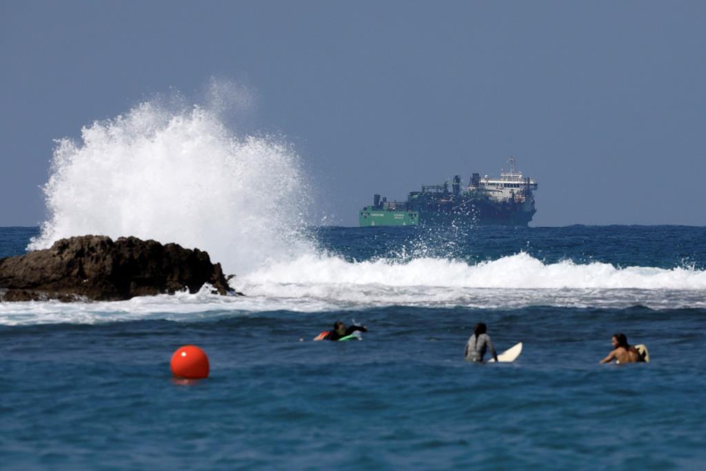People surf as a vessel involved in the construction of a natural gas pipeline is seen behind them in the Mediterranean Sea near Dor Beach, northern Israel August 28, 2018.