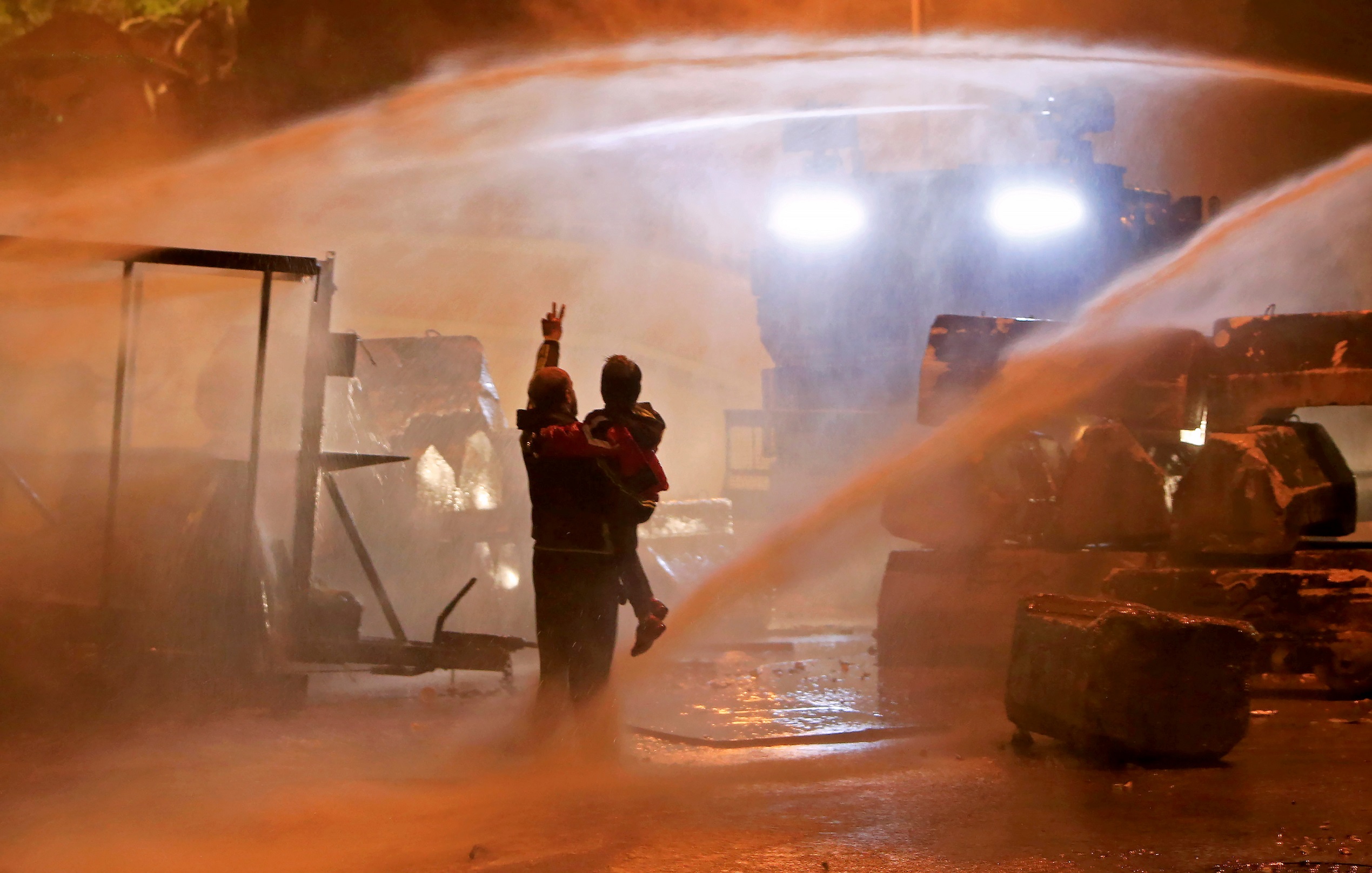 A demonstrator gestures as he holds a child while being sprayed by a water cannon during a protest against the newly formed government outside the government headquarters in downtown Beirut, Lebanon January 25, 2020.