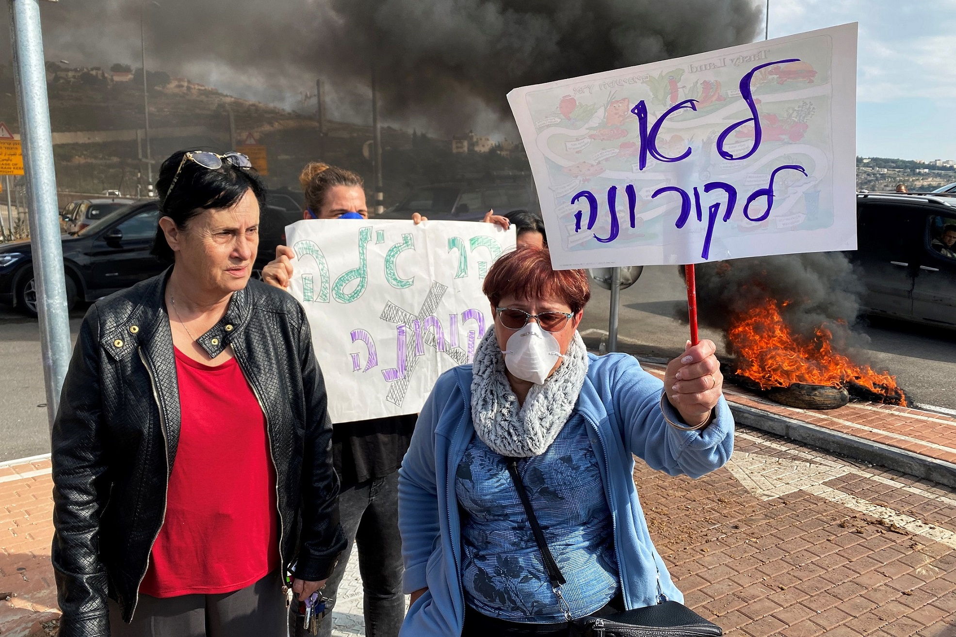 Residents hold placards as they demonstrate against a report that Israel may quarantine visitors from South Korea at a military base in Har Gilo. February 23, 2020. The Hebrew writing reads: