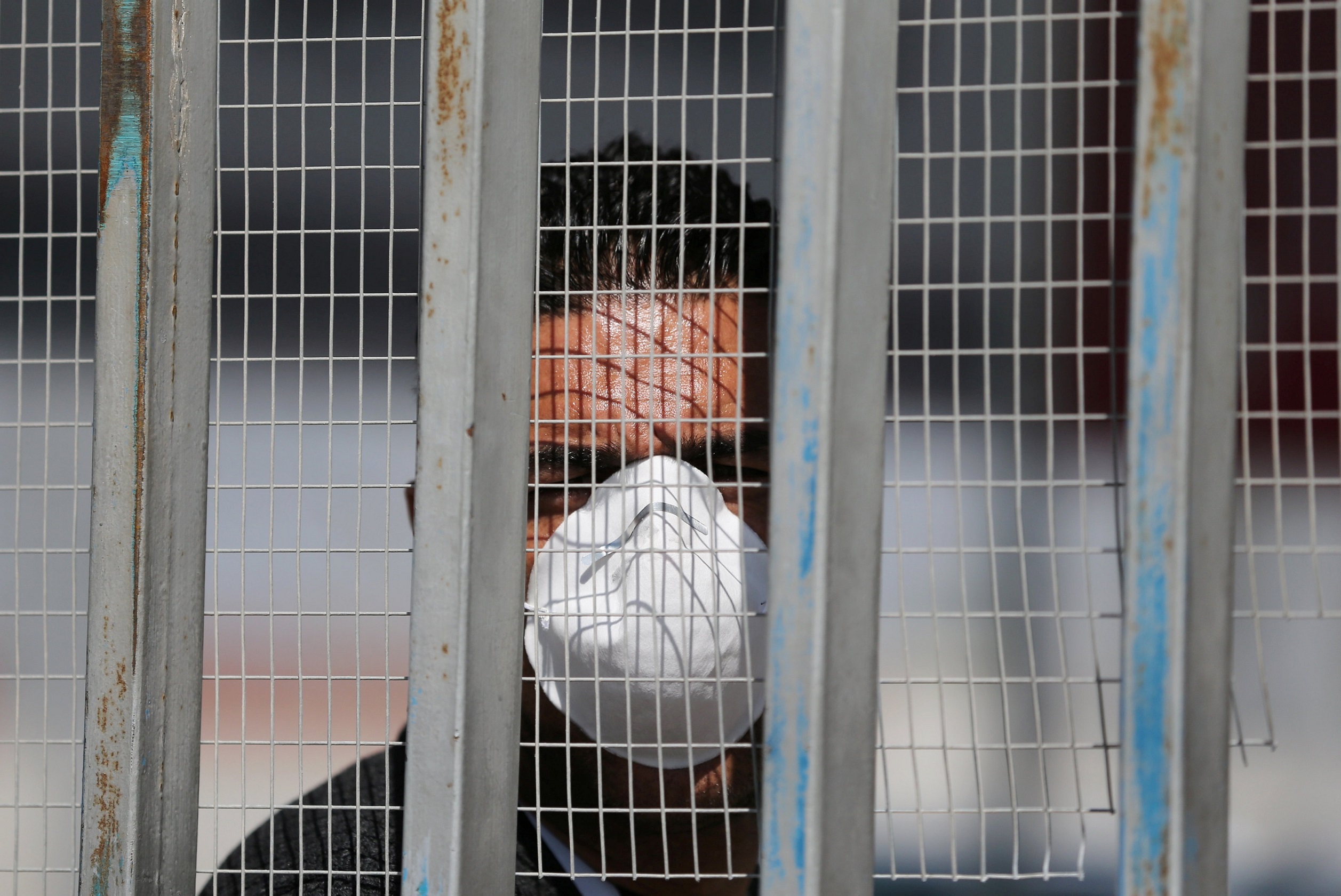 A man, wearing a mask amid coronavirus precautions, looks through a fence as he waits for Palestinians returning from abroad, at Rafa border crossing with Egypt, in the southern Gaza Strip